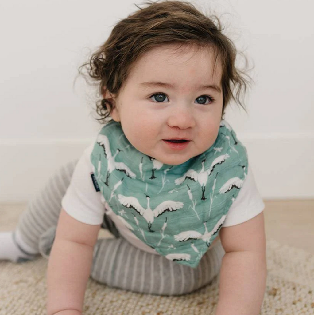 A very cute baby about to crawl wearing the muslin bib with crane pattern.