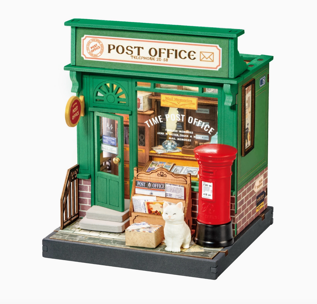 Close up picture of the Century Post Office miniature house with the accessories set up like the little cat, packages and red mailbox. 