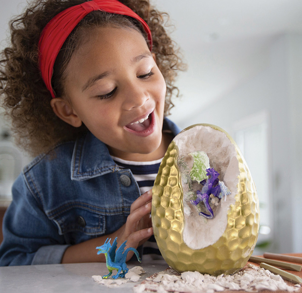 Girl smiling looking at the giant egg with a dragon figure coming out.