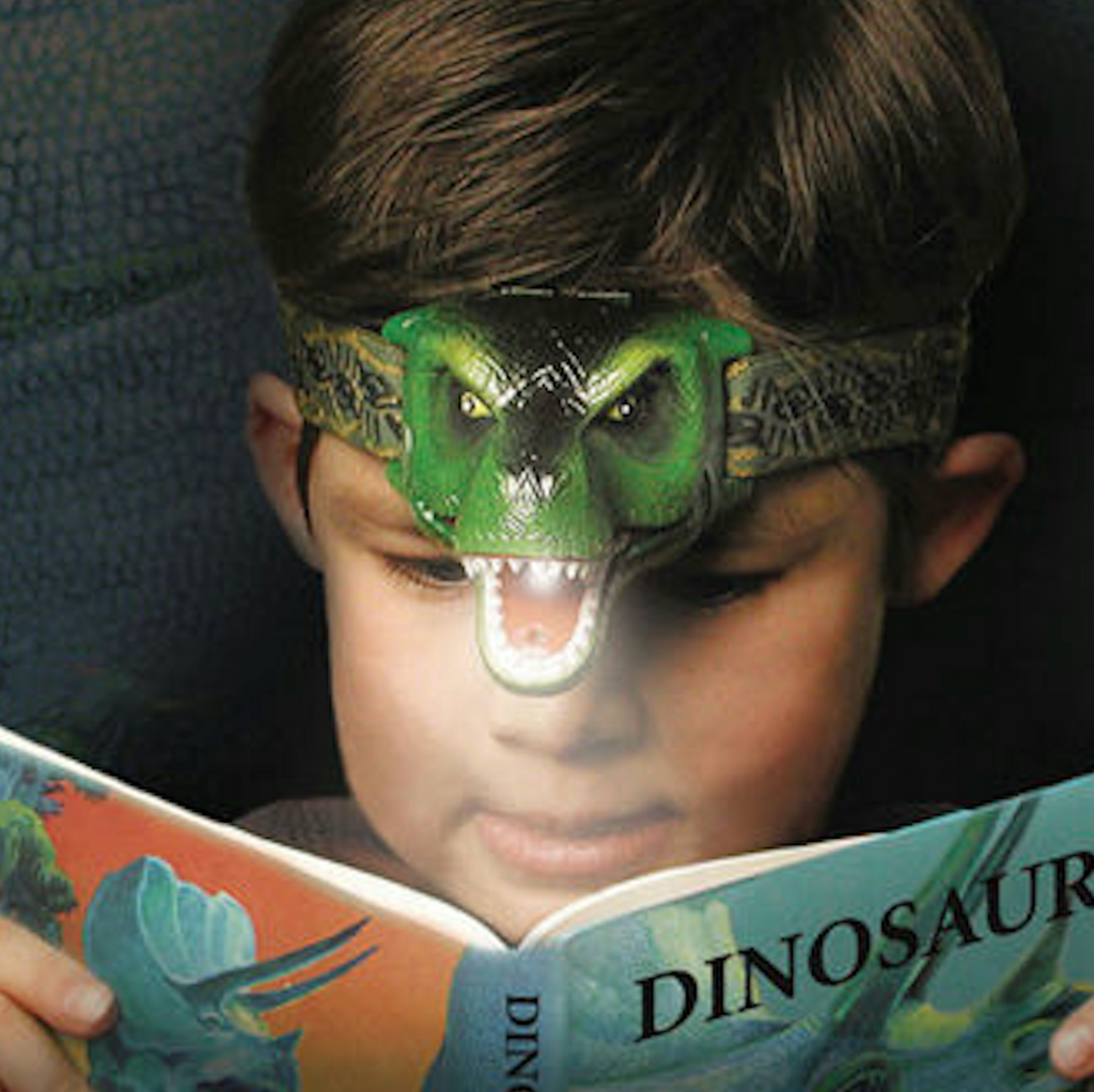 A young child wearing the DinoBryte Headlamp while reading in bed. 