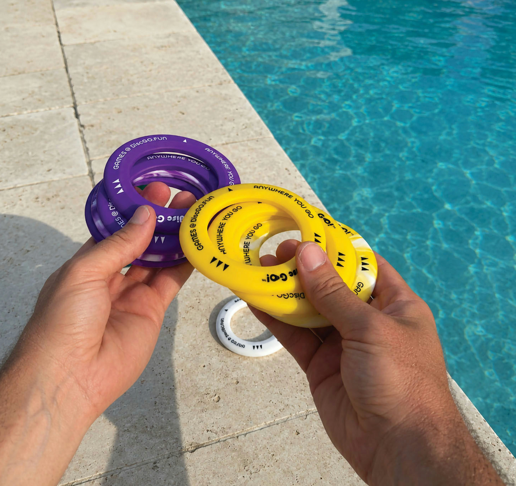A hand holding the Disc Go!  game rings poolside. 