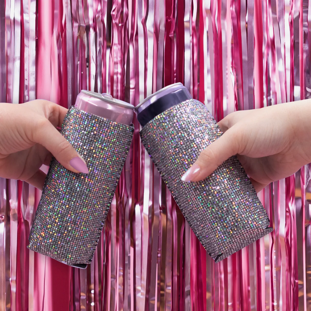 Two hands toasting in front of festive streamers with slim cans inside the Disco Koozie. 