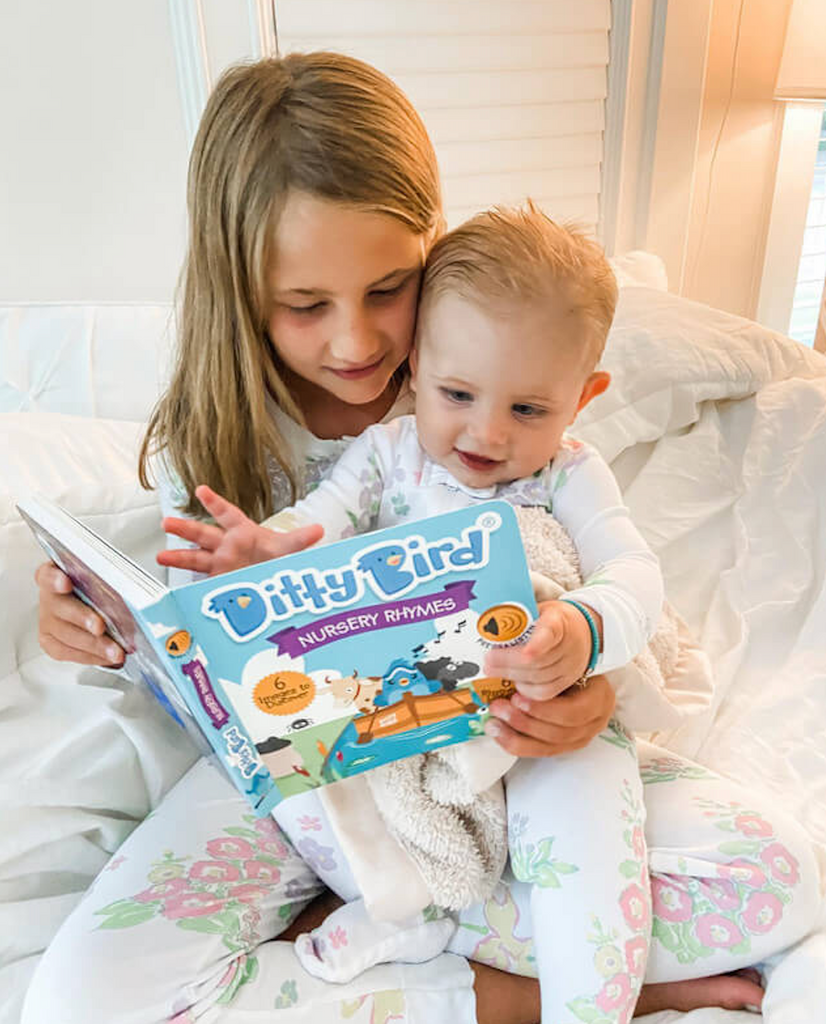 An older sibling reading the Ditty Bird Bedtime Songs book to a toddler. 