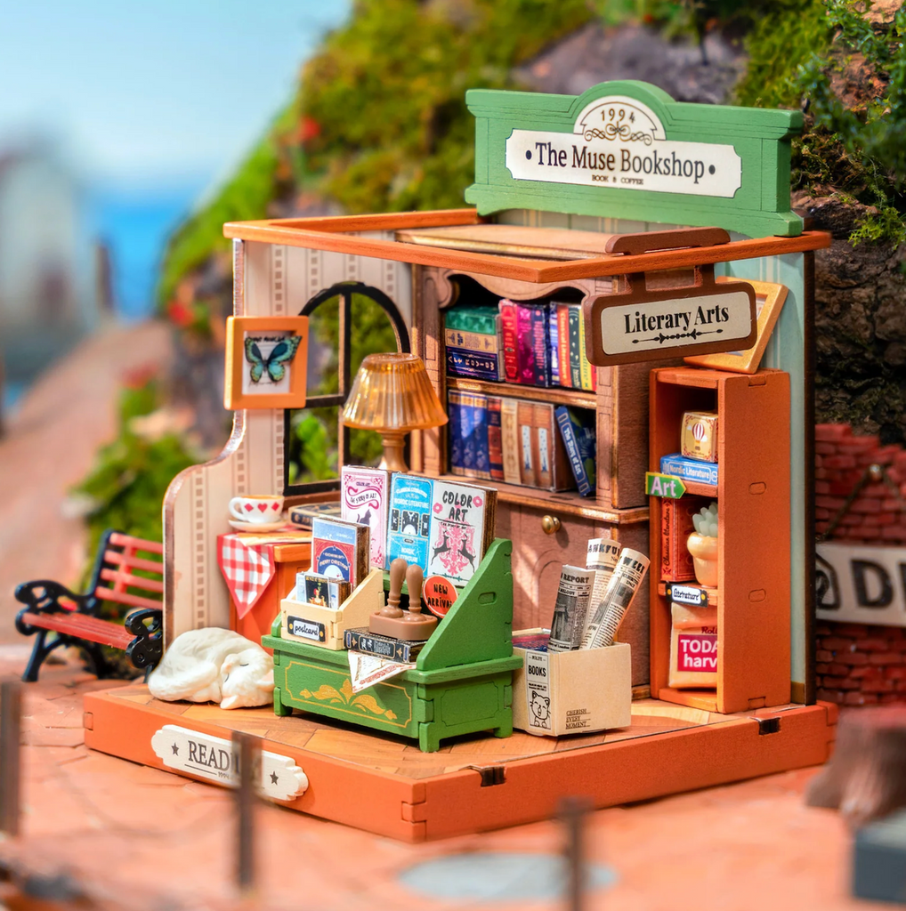 View from the side of The Muse Bookshop Miniature House Kit with it's mini book bin, bookshelves, and newspaper bins. 