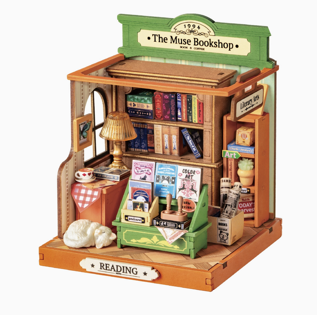 Close up picture of The Muse Bookshop Miniature Model Kit, with miniature versions of books, newspapers,  and even a sleeping cat. 