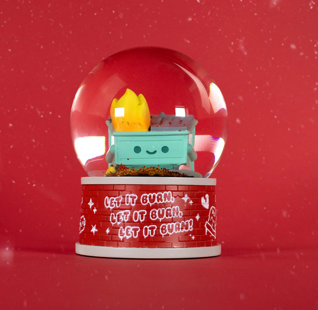 Dumpster Fire snow globe on top of it's base that looks like a brick wall with "Let It Burn" written in white graffiti style lettering in a repeating pattern.