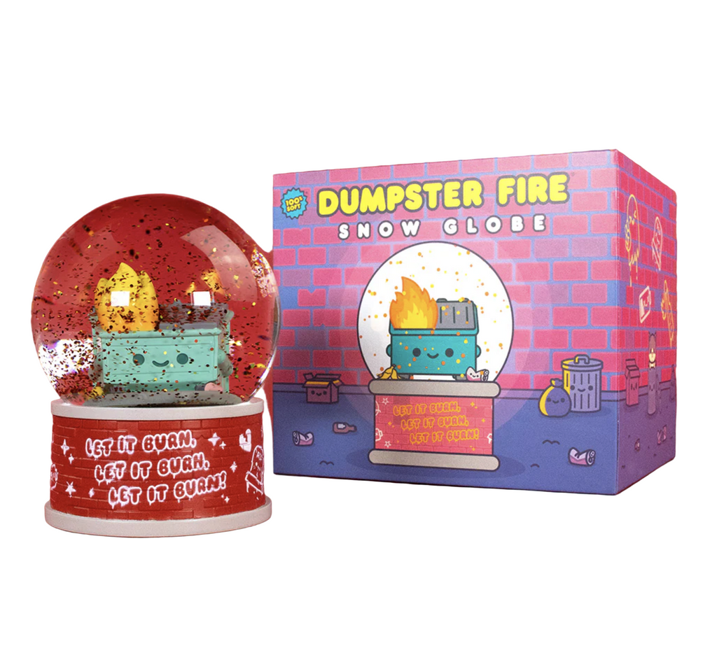 The Dumpster Fire Snow Globe sitting beside it's box, which has an illustrated picture of the Dumpster Fire snow globe set in front of a brick wall. The snow globe has red glitter swirling around the Dumpster Fire character on a brick wall base that reads "Let It Burn" in a repeating pattern. 
