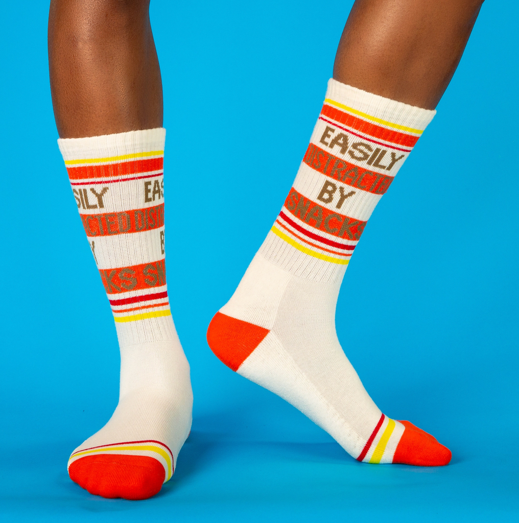 A person wearing the "Easily Distracted By Snacks" crew socks, pictured on a blue background. 