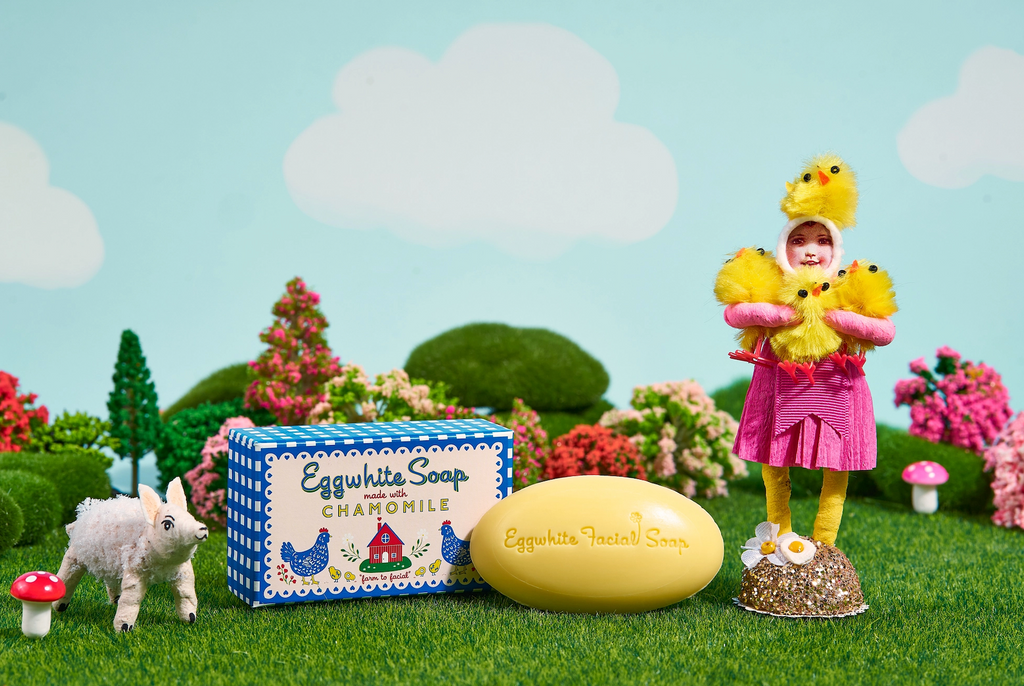 Egghwhite and Chamomile Soap with a doll in a duck costume and small sheep figure in a decorative outdoor scene. 