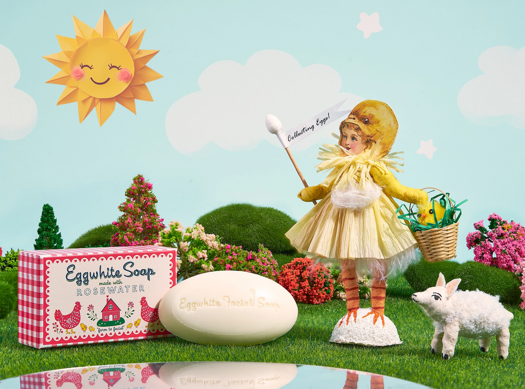 The Eggwhite and Rosewater soap in a decorative scene with beautiful flowering bushes, a sheep and a doll in a baby chick costume. 