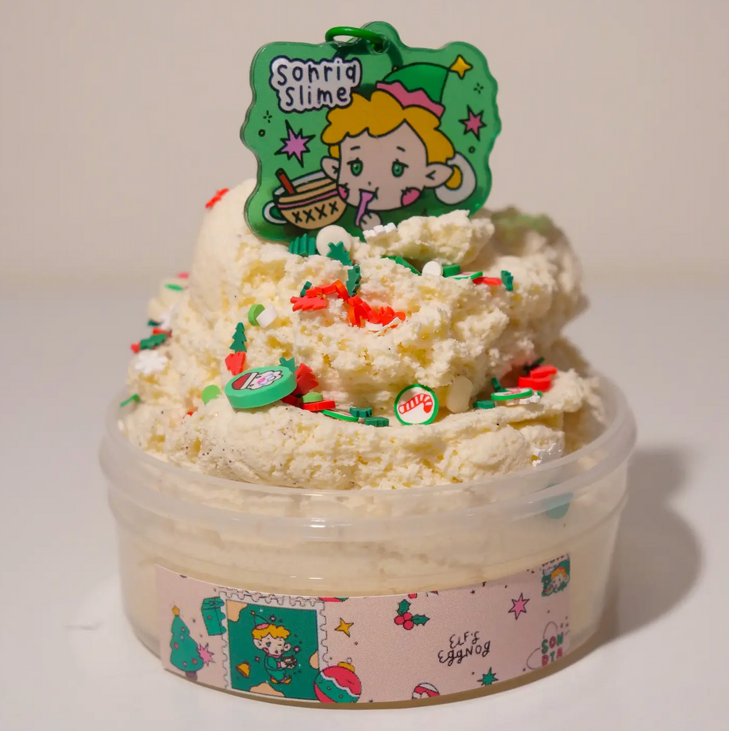 A key chain with an illuistrated Elf sipping on egg nog sitting atop a fluffy pile of scented slime in a tub. (Not food)