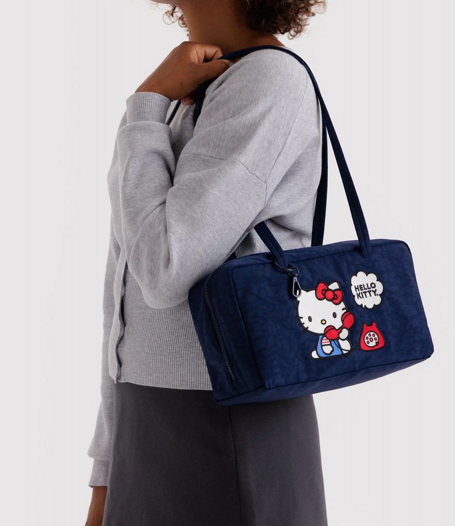 Person holding the Baggu navy blue bowler bag with Hello Kitty design embroidered on the side. 