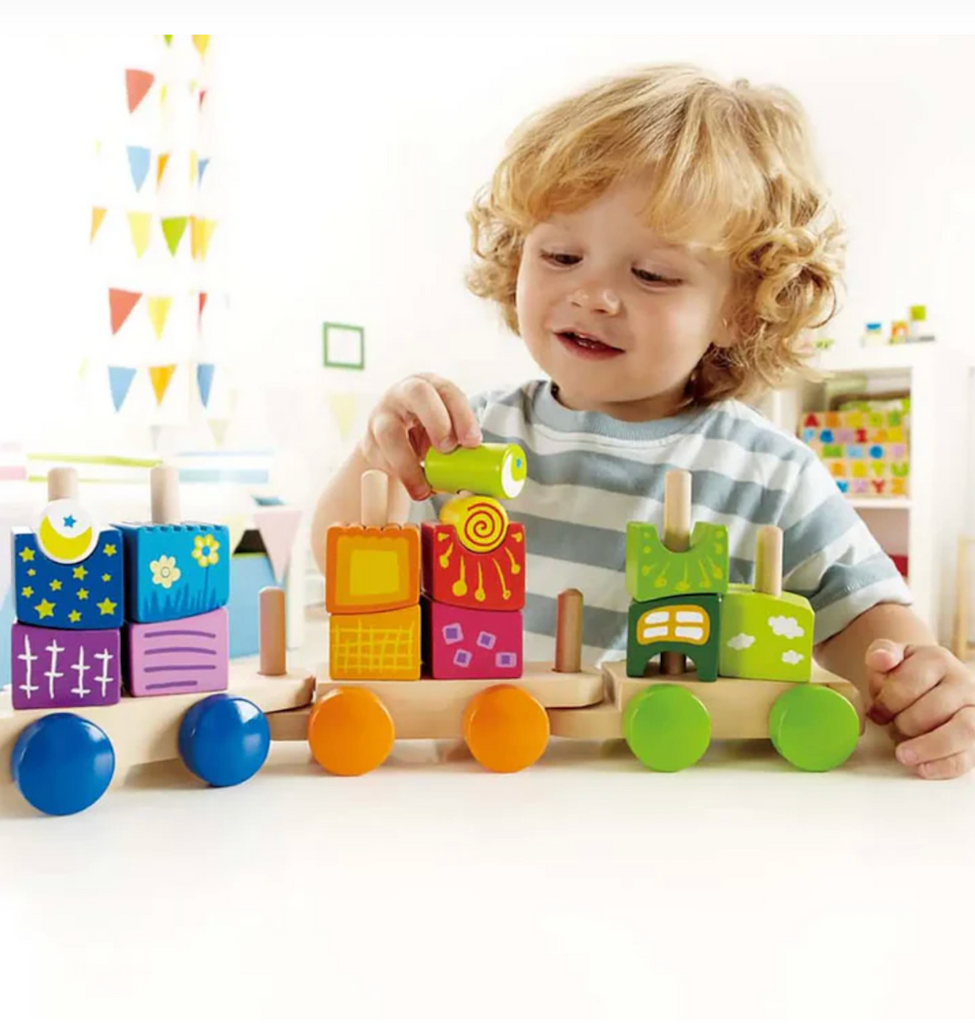 Child playing with the Fantasia Blocks Train, stacking the brightly colored blocks and pulling the train along a table. 