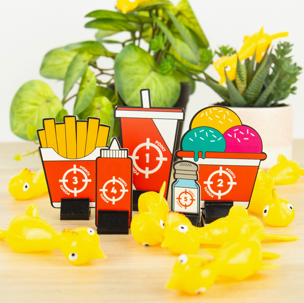 Set of colorful toy food items with standees on a light surface with plants in the background