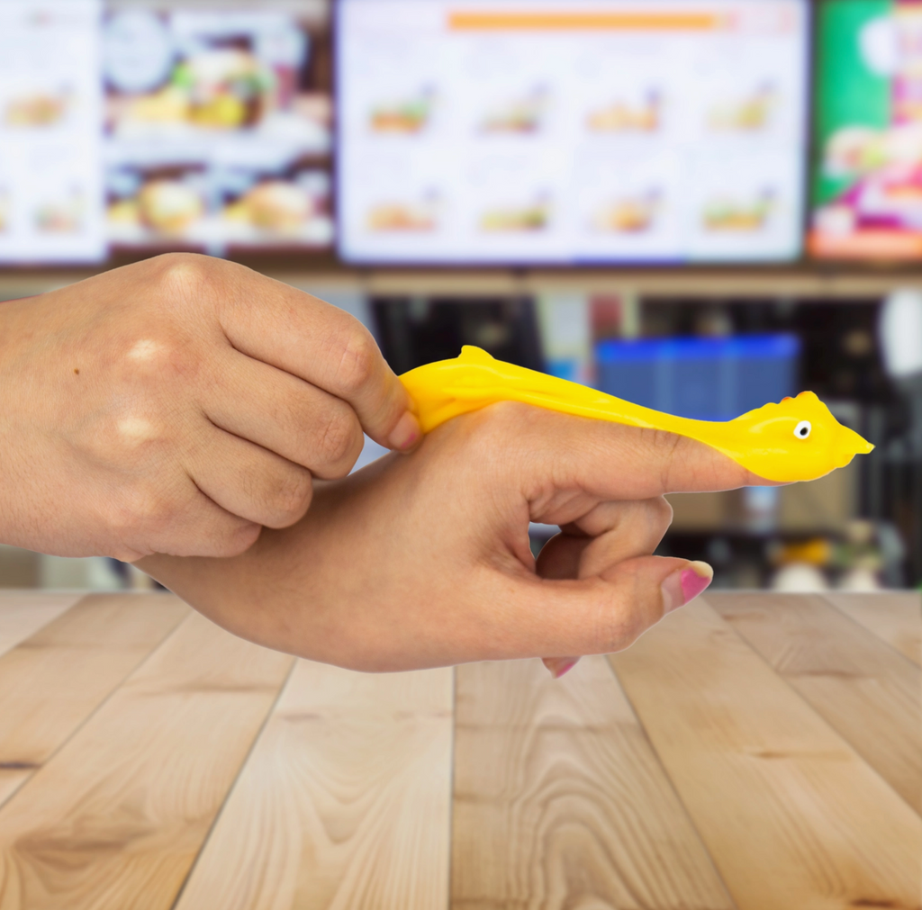 Person holding a yellow rubber chicken toy with a blurred restaurant interior in the background