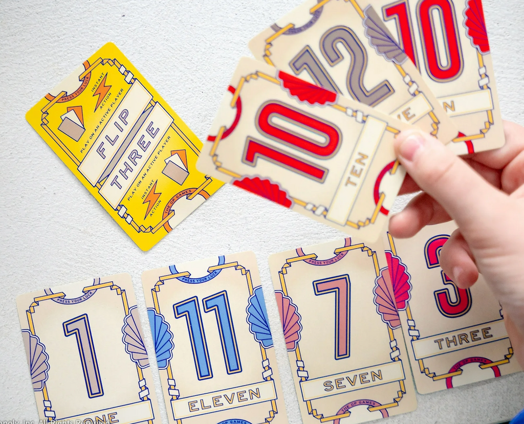 Cards with colorful numbers illustrated on one side laid on the table and a person holding three cards in their hand. 