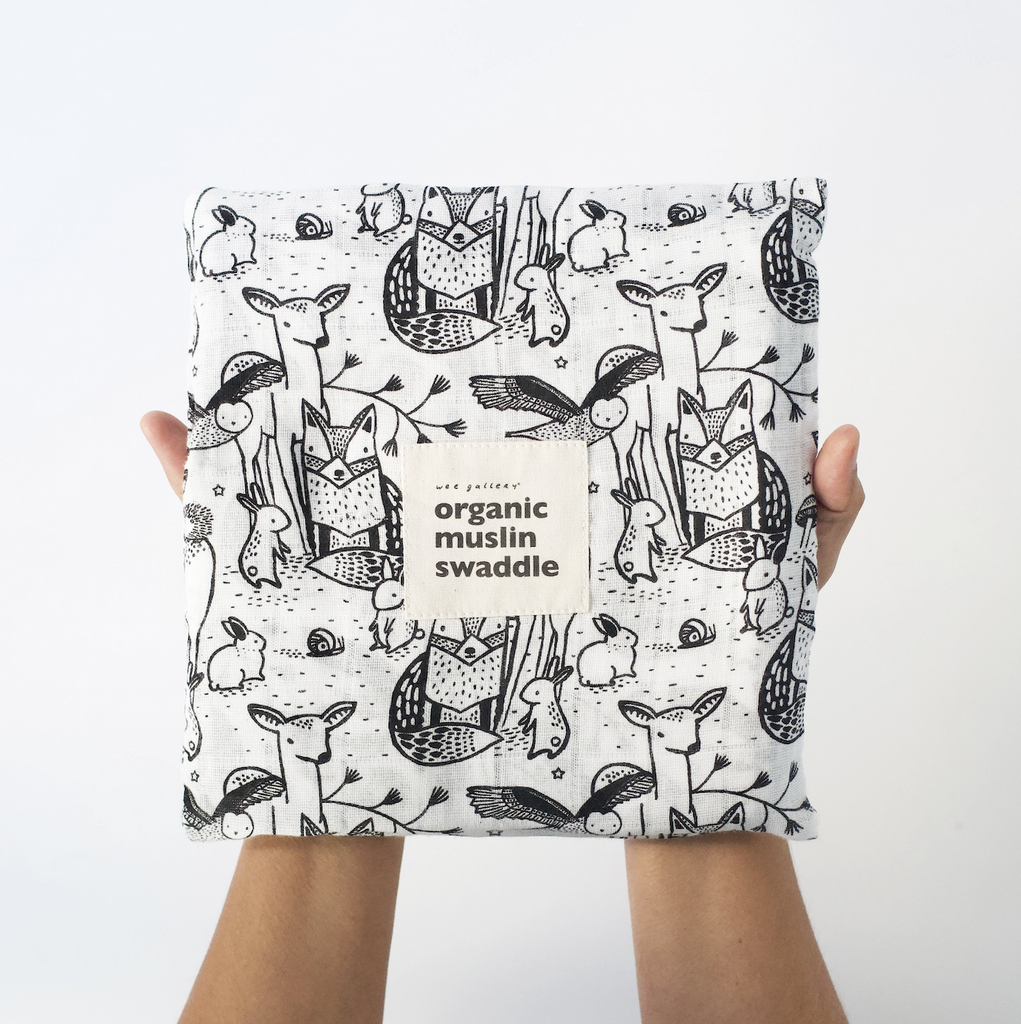 The Organic Muslin Swaddle blanket with forest themed animals printed all over it, folded into a square. 