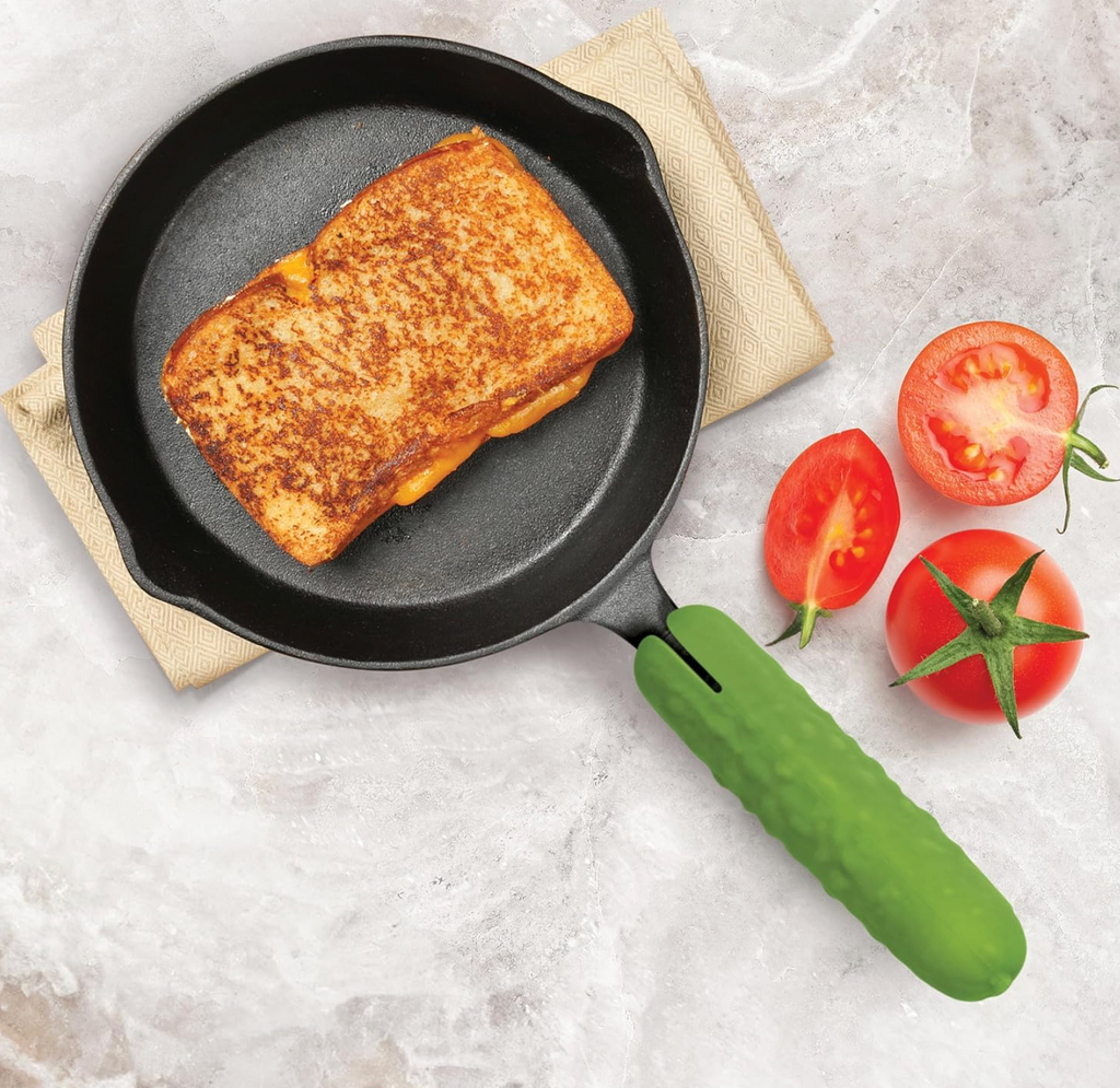 A frying pan with a grilled cheese sandwich inside and the pickle shaped pan handle cover. 