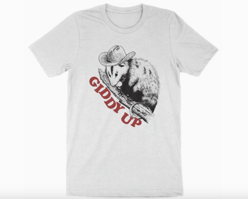 Illustrated sketch of a possum wearing a cowboy hat perched on a branch that reads "Giddy Up" on a white shirt. 