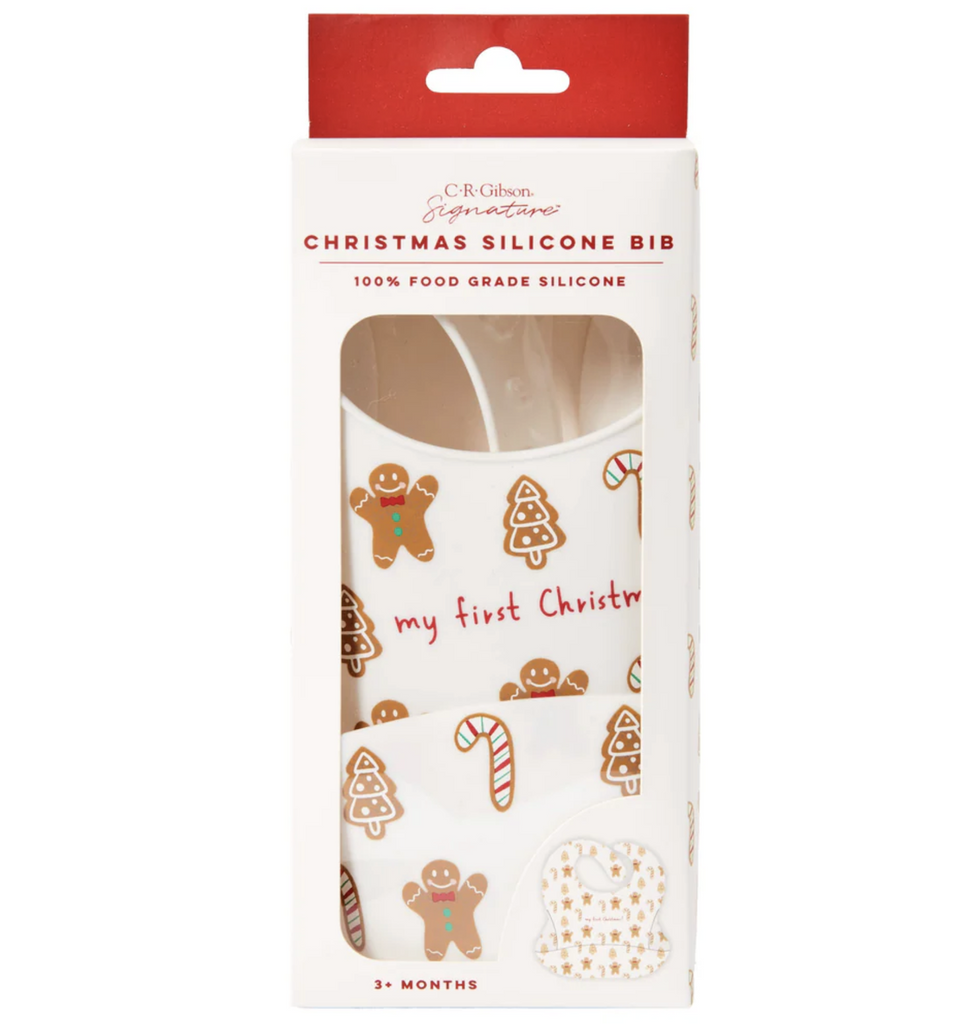 Ginger Cane Silicone Bib rolled up and packaged in a box with a clear window to show off the gingerbread men, Christmas trees and candy canes that decorate the bib. The bib also reads "My first Christmas" 