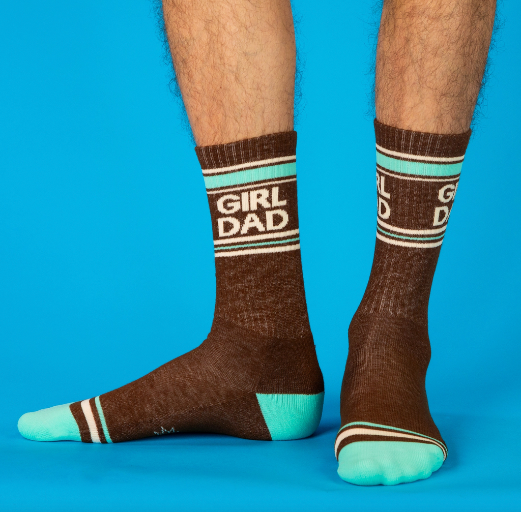 Someone wearing brown and turquoise crew socks that read "Girl Dad" 