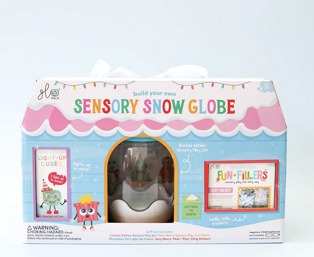 The Glo Pals Snow Globe Gift Set packaged in a box that looks like a cute cottage with snow on the roof. Each of the items included in the set can be seen through windows in the box. 