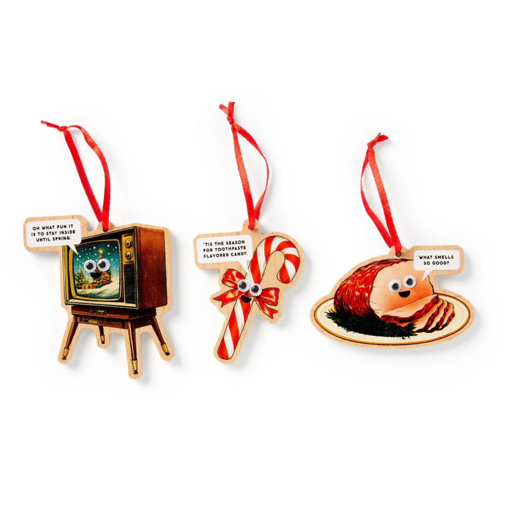 Three Christmas ornaments shaped like a TV, candy cane, and pie all with googly eyes and a witty comment attached. Each has a red ribbon to hang on the tree. 