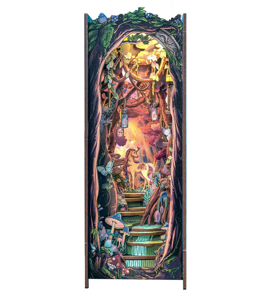 A close up view of the inside of the Grace of the Forest Miniature Book Nook model kit clearly showing  the beautiful unicorn at the top of rocky steps under a canopy of trees. 