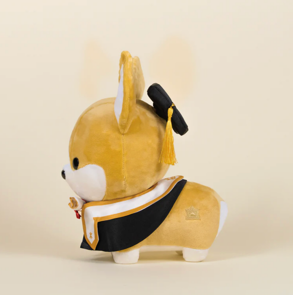 The Graduation Corgi stuffed animal viewed from the side, with his graduation cap and gold tassel hanging down on the side. 