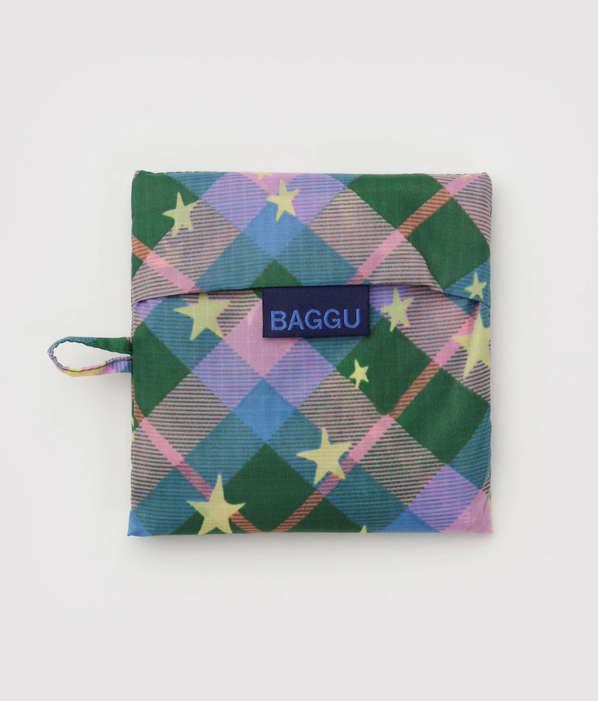 Baggu standard shopping bag folded flat in it's storage pouch with a purple, pink and green pattern with gold stars. 