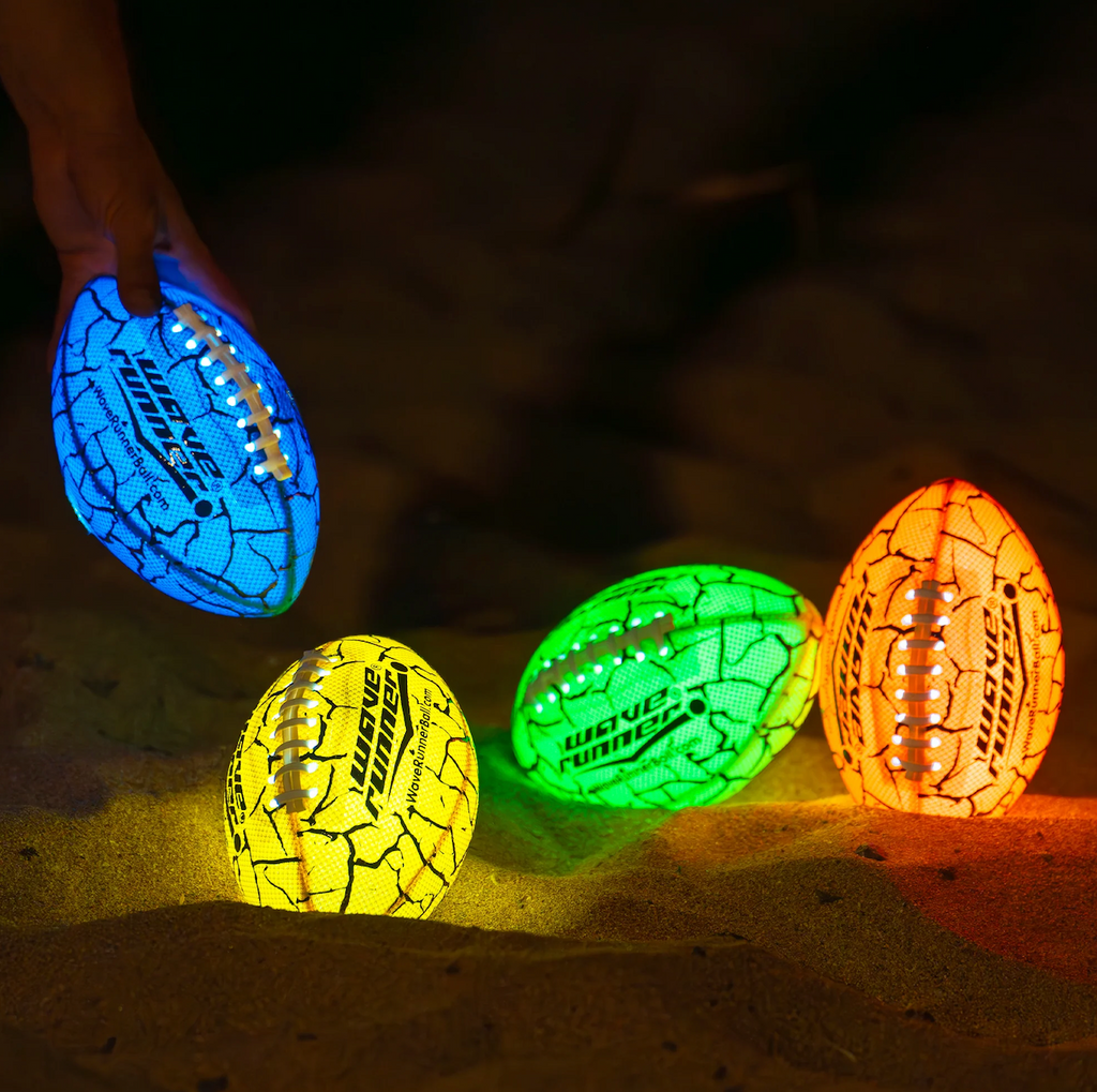 Assorted colors of the Grip It Led Wave Runner American Football all lit up and glowing in the dark. Colors shown are blue, yellow, green and orange. 
