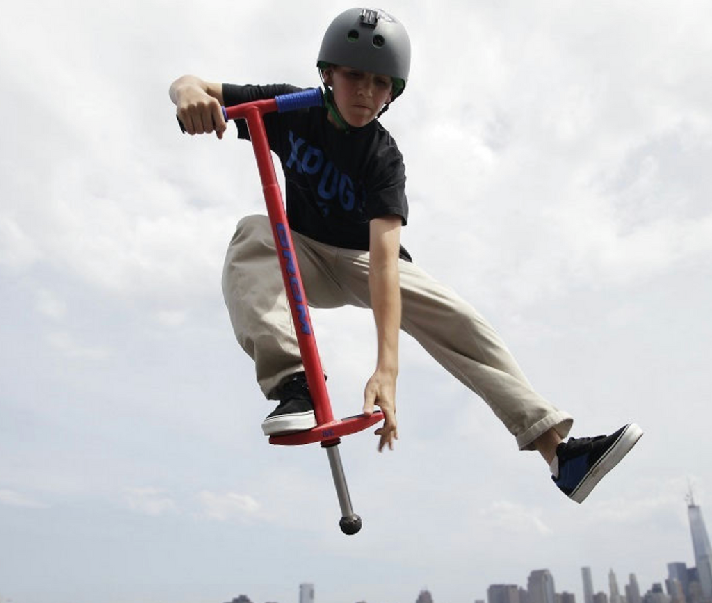 A kid in the air preforming a trick on the Grom Pogo Stick in red. 