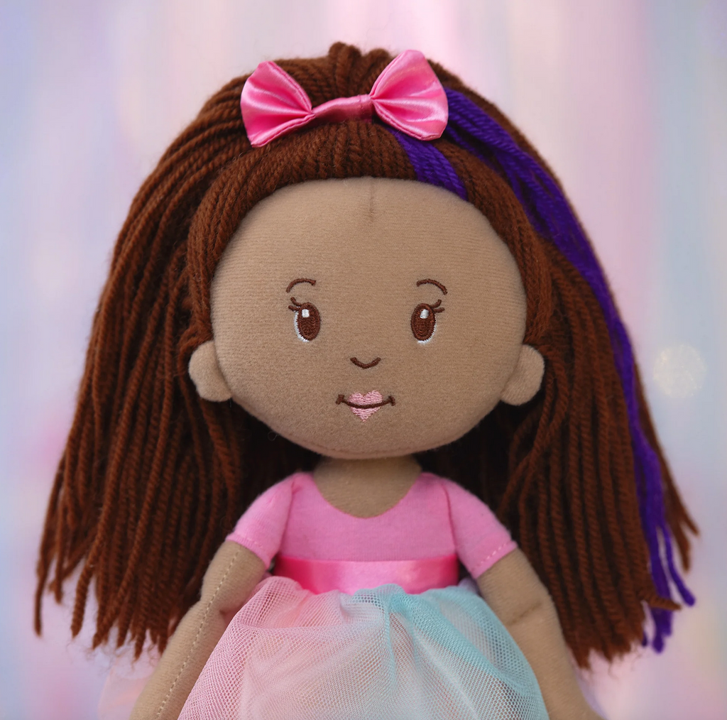 Groovy Girls doll Iris a plush doll with brown skin, brown hair, pink bow, and pink dress and tutu. 