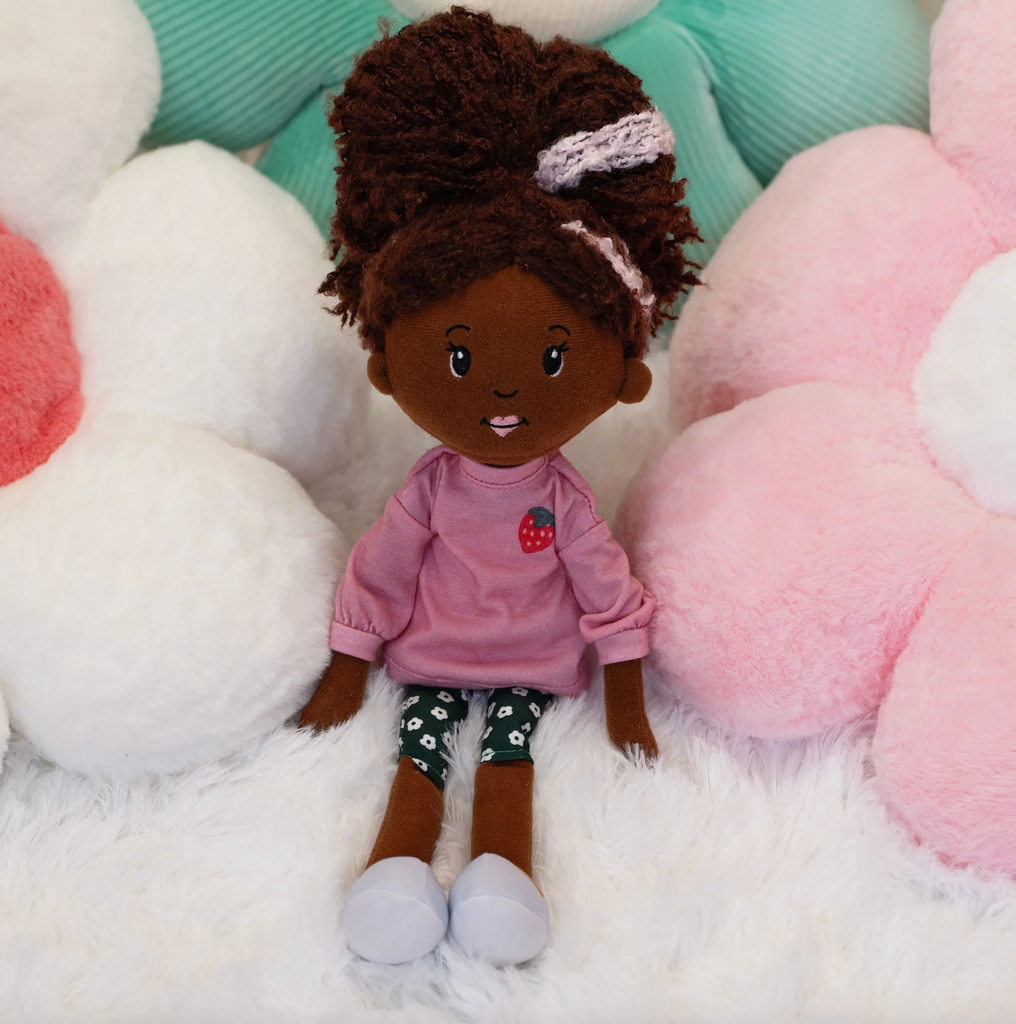 Groovy Girls doll Saige a dark brown skinned plush doll sitting on a fuzzy blanket. 