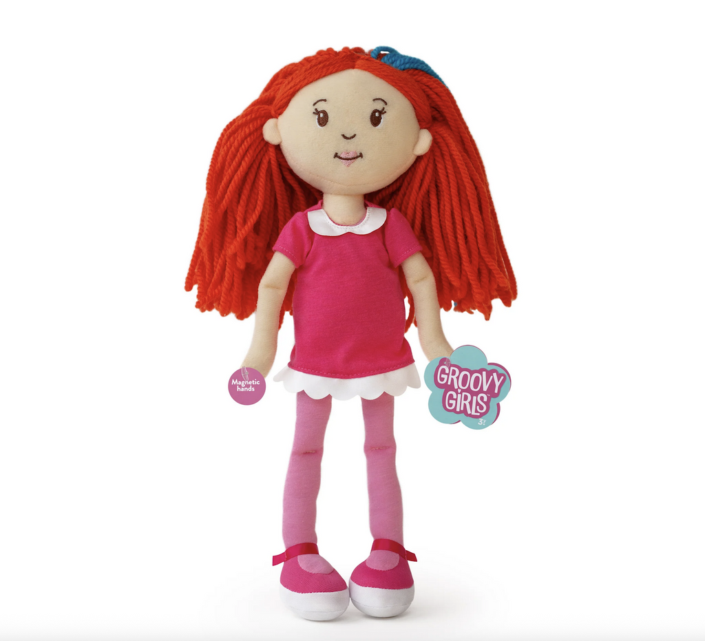 Groovy Girls doll Poppy, a soft bodied baby doll with bright red hair. She is wearing a pink shirt with a white ruffle at the bottom. 
