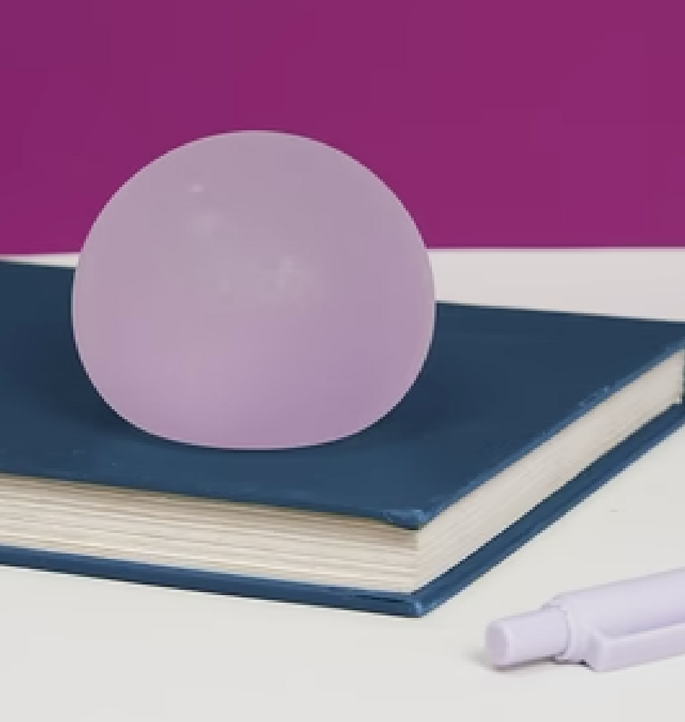 The Gump stress ball in Mist sitting on top of a book on a desk. 
