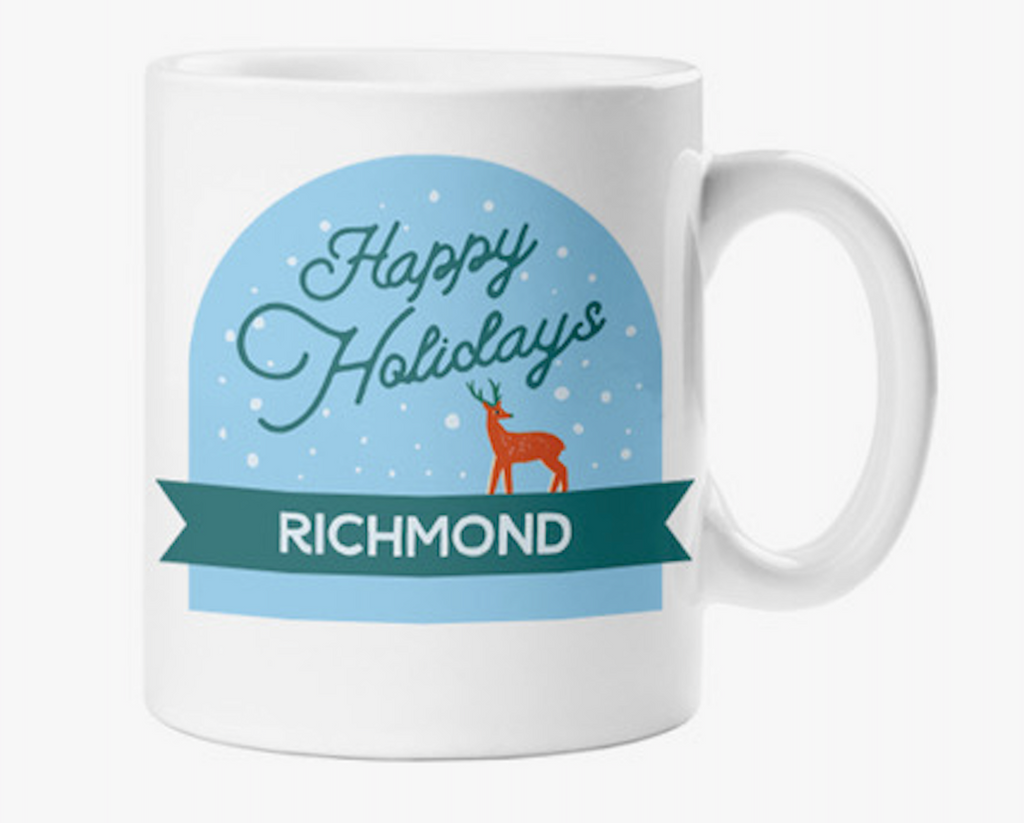 White ceramic mug decorated with a snow globe design that has a red silhouette of a deer against a blue backdrop. It reads "Happy Holidays, Richmond"