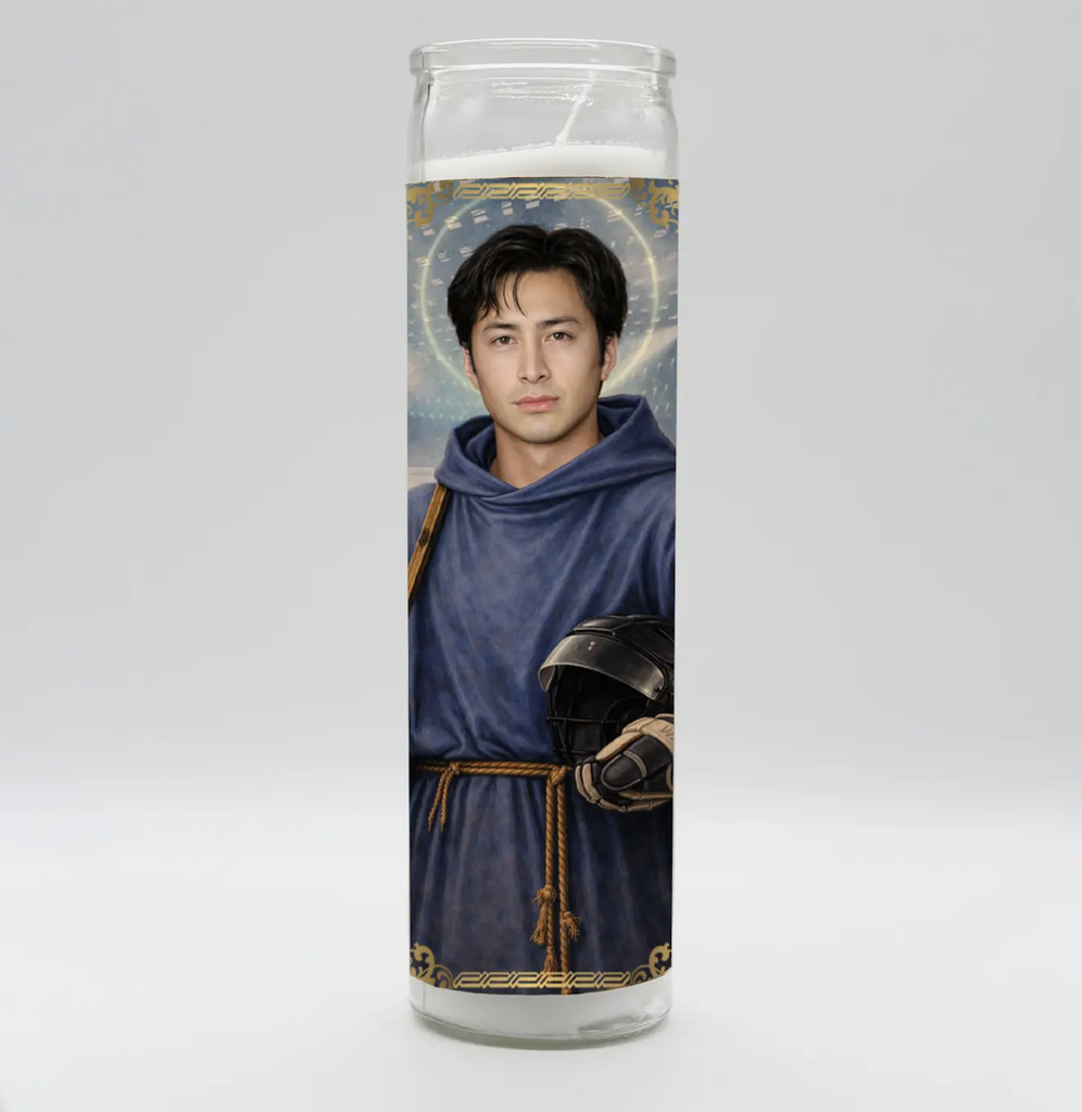 Shane Hollander from Heated Rivalry dressed as a saint in a blur robe and holding a hockey helmet pictured on the front of a tall white prayer candle. 