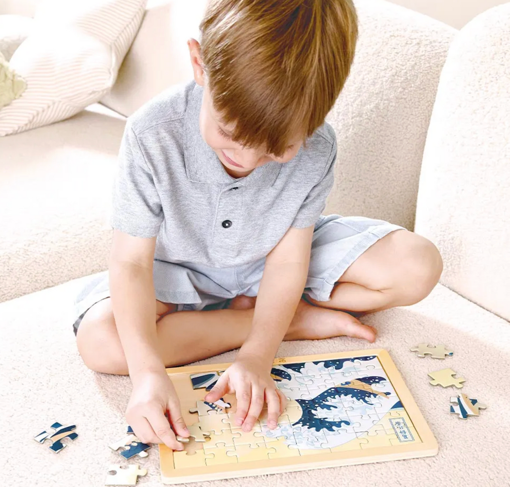 A young child sitting on a couch and putting the Great Wave Wooden puzzle. 