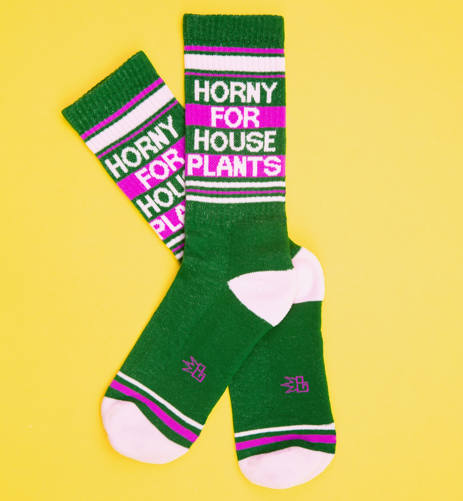 A pair of dark green tube socks with white and fuschia stripes that read "Horny For House Plants" in white letters. 