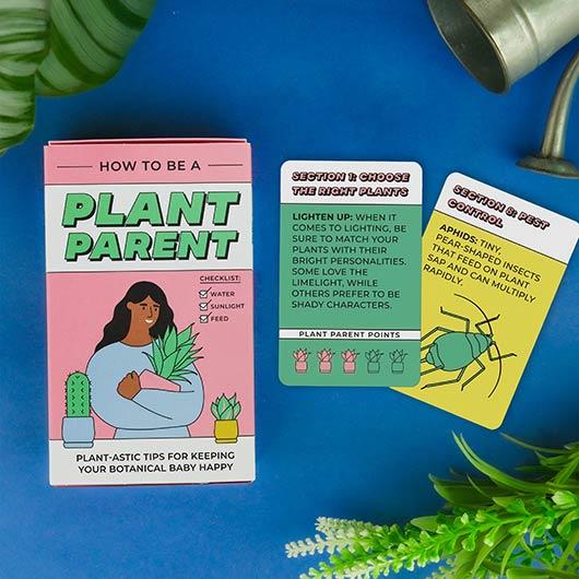 Cover of "how To Be a Plant Parent" deck with illustration of a woman hugging a potted plant. There are two colorful tip cards laid out beside the deck.