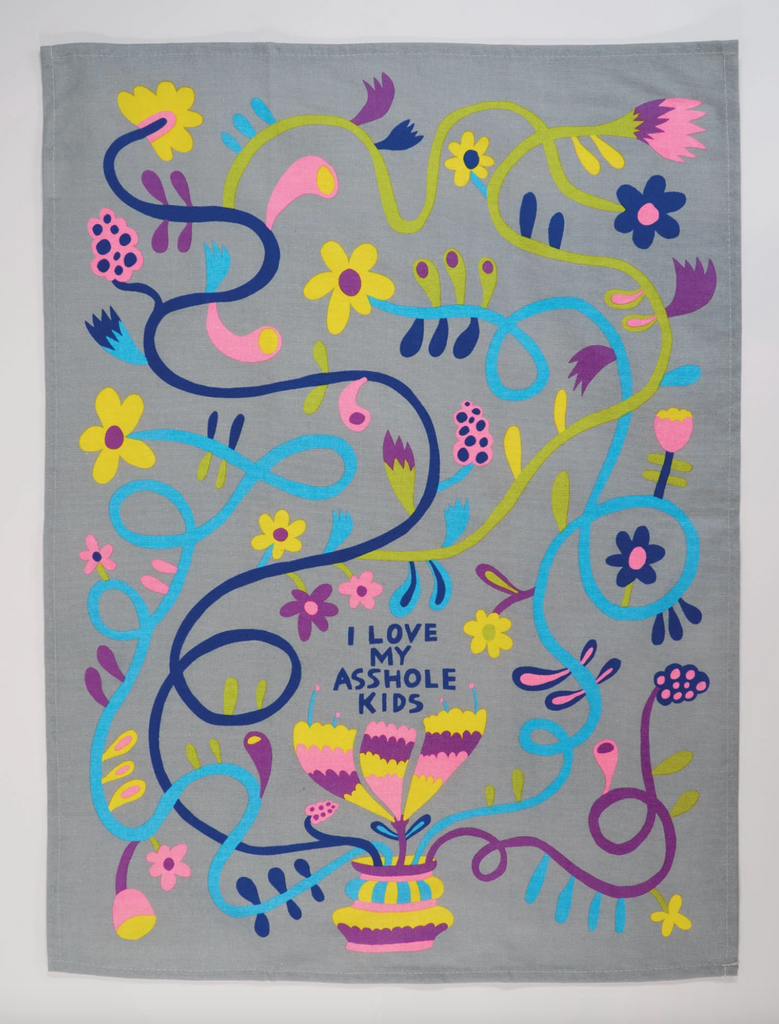 Gray dish towel unfolded and laying flat with a floral pattern all over that reads "I Loce My Asshole Kids"