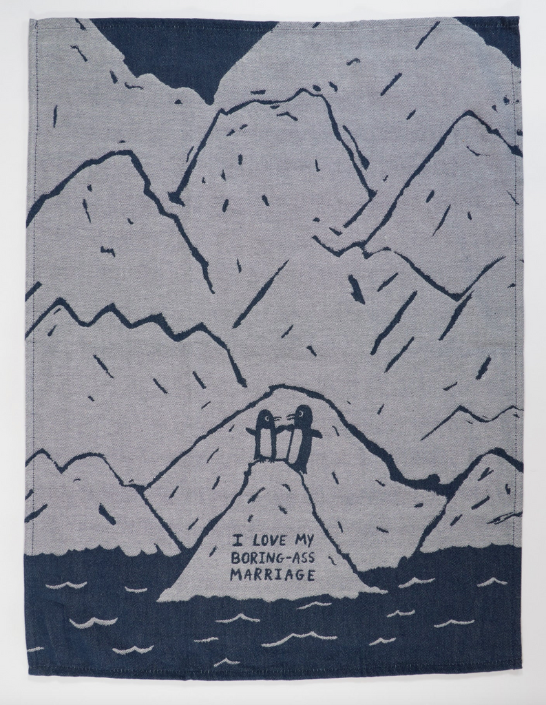 Denim blue woven dish towel laying flat with illustration of two penguins on an iceberg with larger icebergs behind them. 