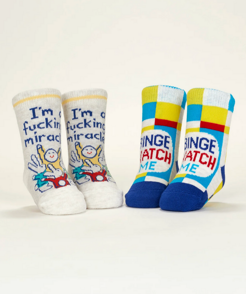 Baby socks displayed on mannequin feet with one pair that reads "I'm a fucking miracle" and the other reading "Binge Watch Me" 