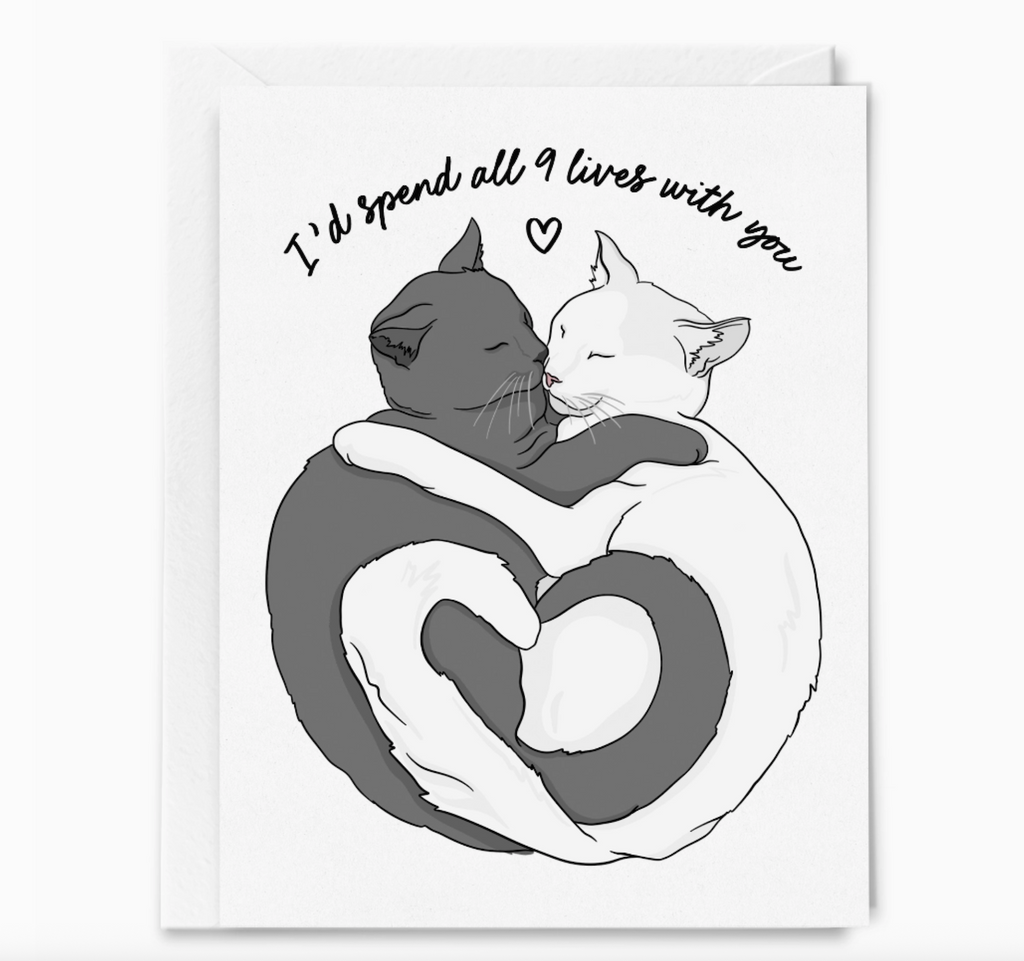 A greeting card with an illustration of a grey cat and a white cat snuggling together to form a heart that reads "I'd spend all 9 lives with you" 