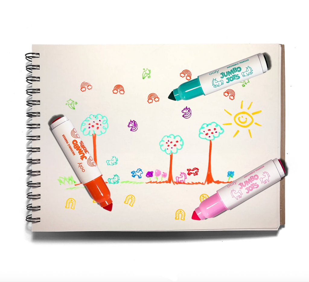 A spiral-bound notebook page with colorful hand-drawn cartoon trees, and stamps of rainbows, and unicorns with three Jumbo Jots Unicorn markers. 