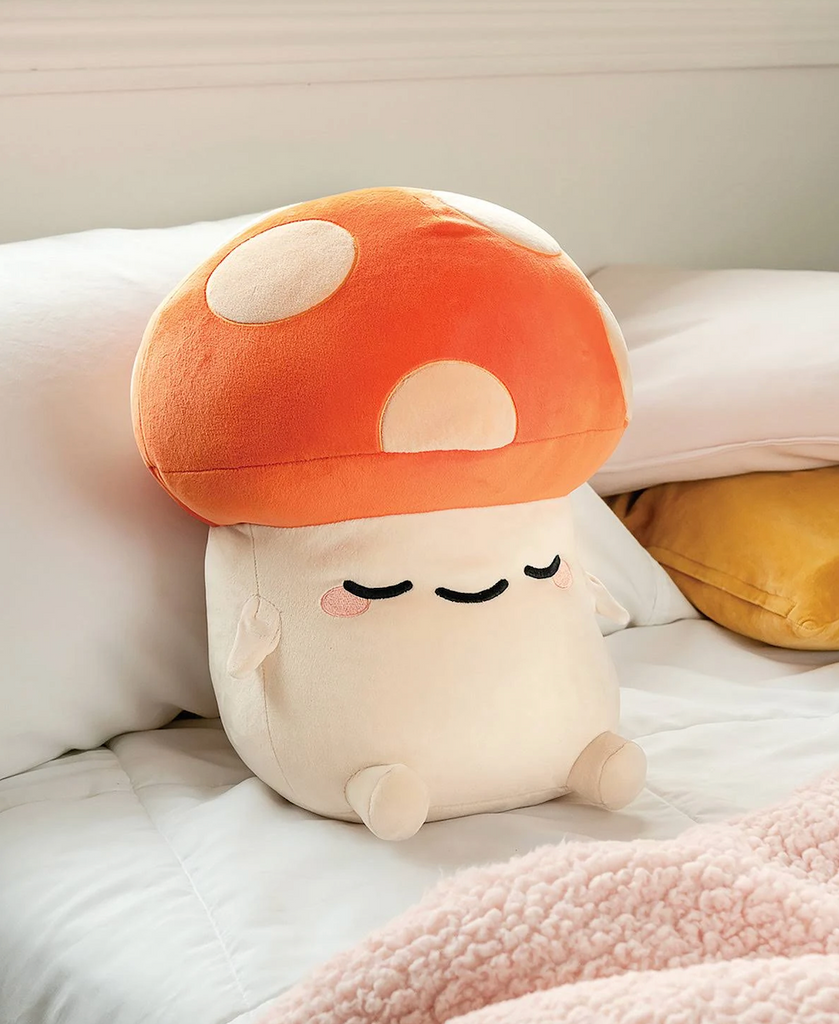 Kai Mushroom Mochi Plush nestled adorably on a bed with the pillows. 