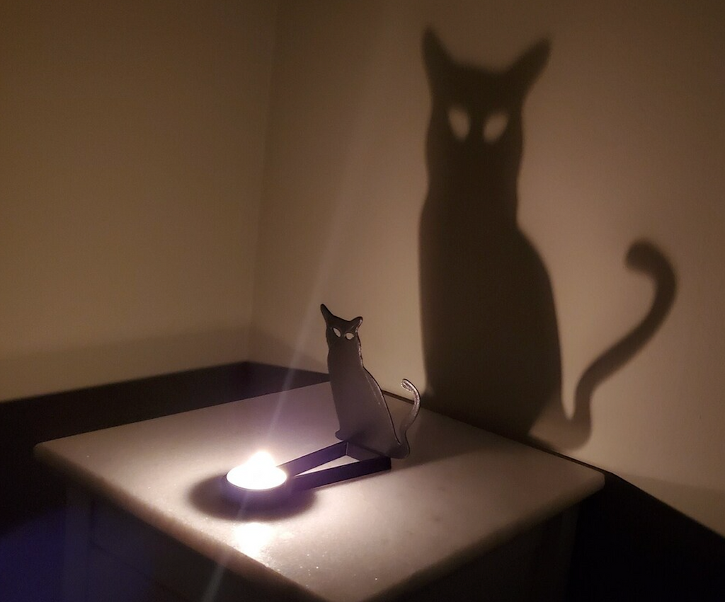A tea light candle lit and placed in the Kealite Cat Shadow Caster creating a shadow of the cat on the wall. 