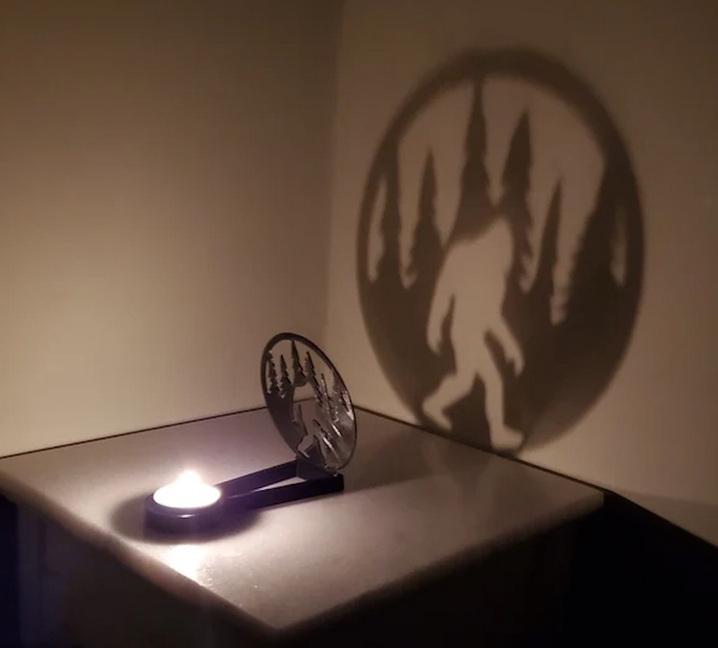 Kealite Bigfoot Shadow Caster with a lit candle creating a shadow of Bigfoot walking amongst tress on the wall. 