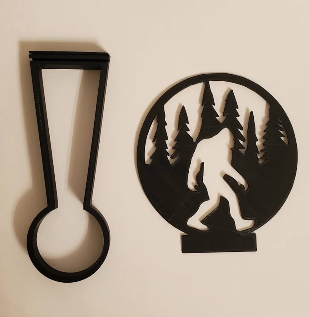 Kealite tea light holder and Bigfoot shadow caster lying flat so that the design of Bigfoot walking amongst trees is clear. 